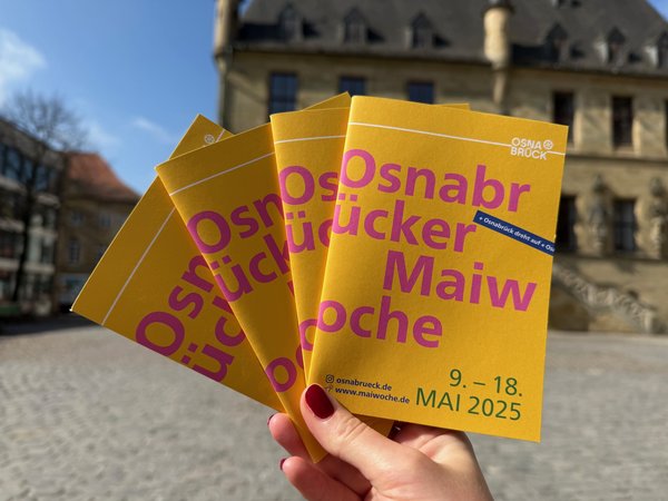 Hand mit dem Programmheft der Maiwoche 2025