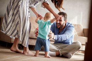 Mutter und Vater führen ihr kleines Kind an den Händen im Wohnzimmer